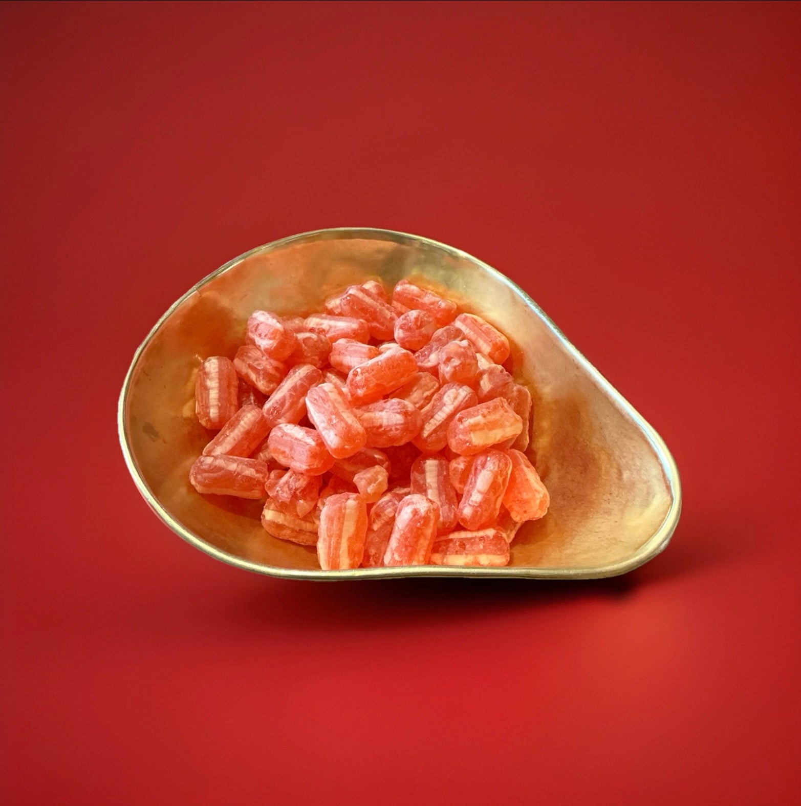 Cough Candy twist are hard boiled sweets with a red and pale orange stripe in a gold bowl with a red background 