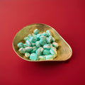 Green and white striped lime flavoured oval shaped soft rock sweets in a gold bowl on a red background 