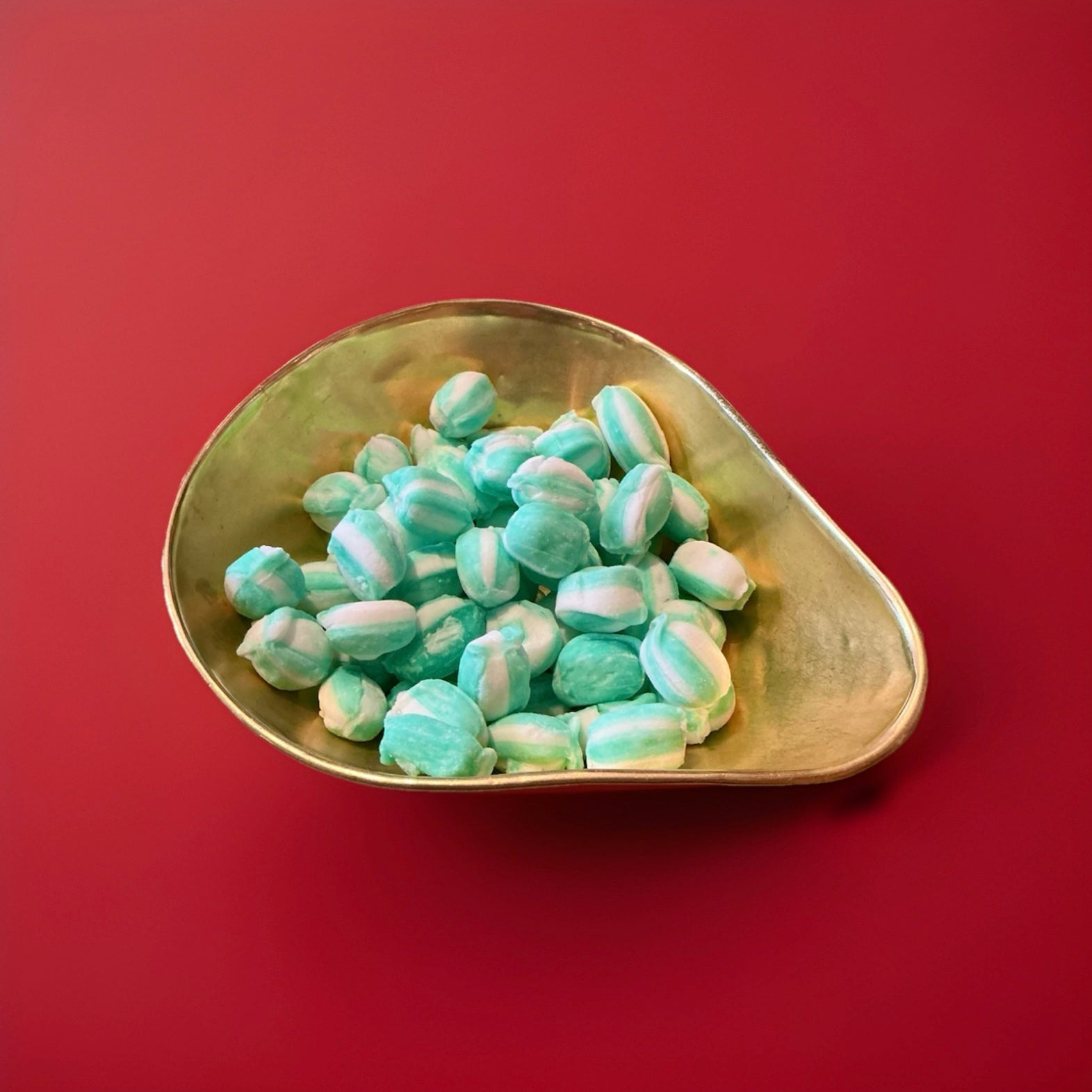 Green and white striped lime flavoured oval shaped soft rock sweets in a gold bowl on a red background 