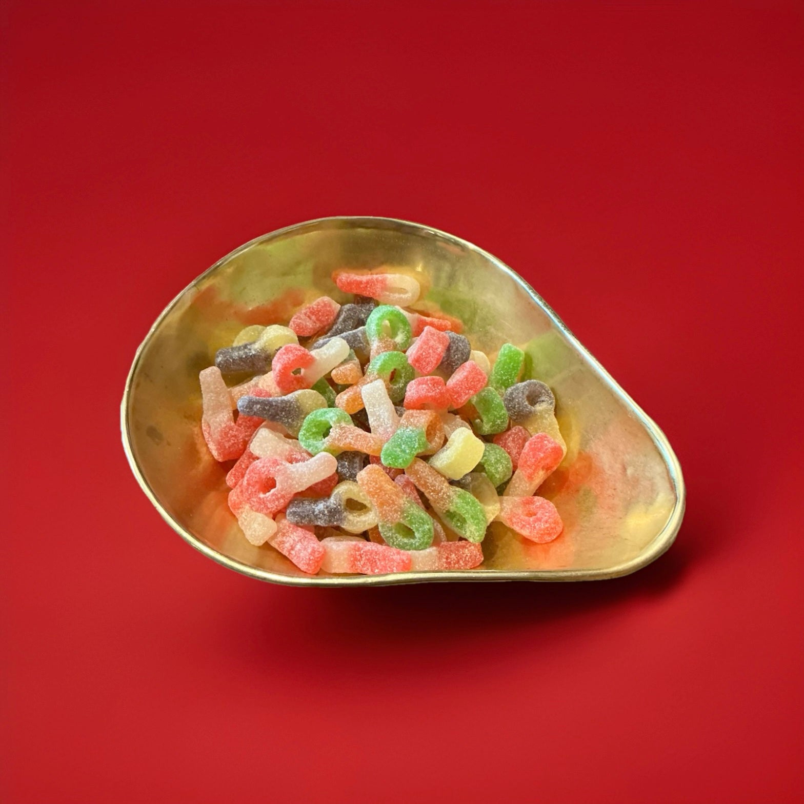 Multicoloured dummy shaped jelly sweets with a sour sugar coating in a gold bowl with a red background 