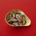 Yellow banana flavoured marshmallow covered in milk chocolate in the shape of a banana in a gold bowl on a red background 