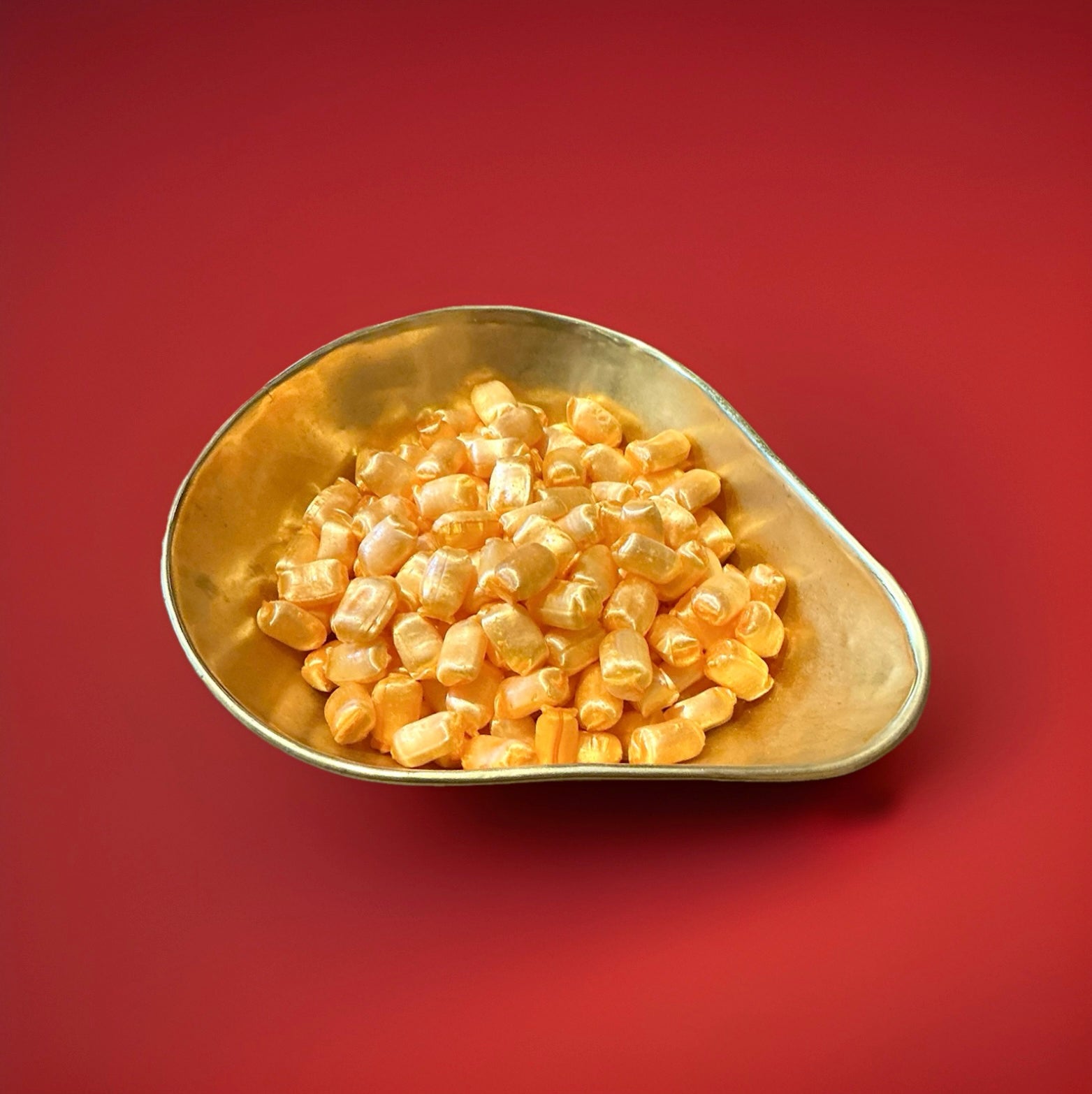 Iron brew flavoured hard boiled orange coloured sweets in a gold bowl with a red background 