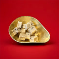 Large pieces of rum and raisin flavoured fudge in a gold bowl with a red background 