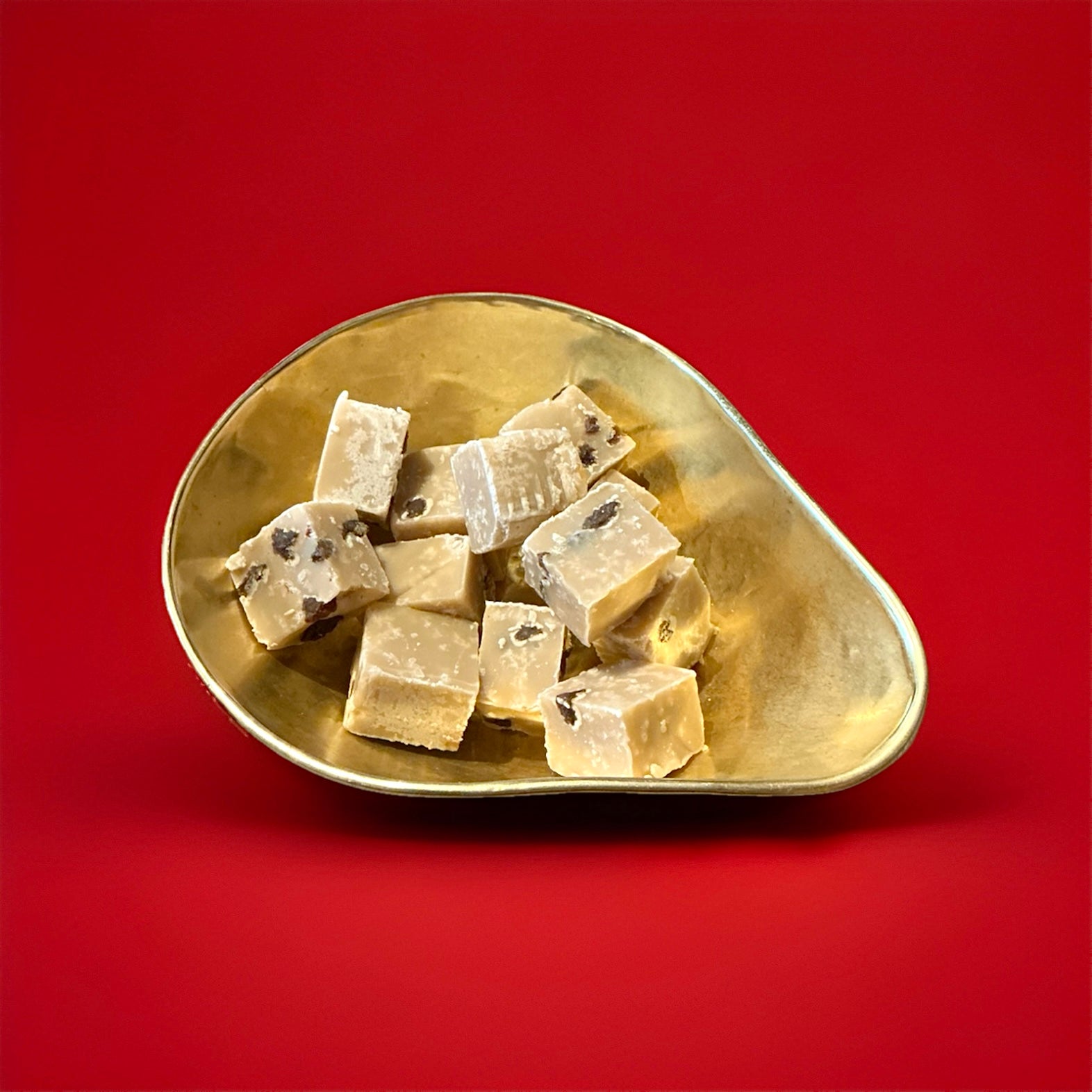 Large pieces of rum and raisin flavoured fudge in a gold bowl with a red background 