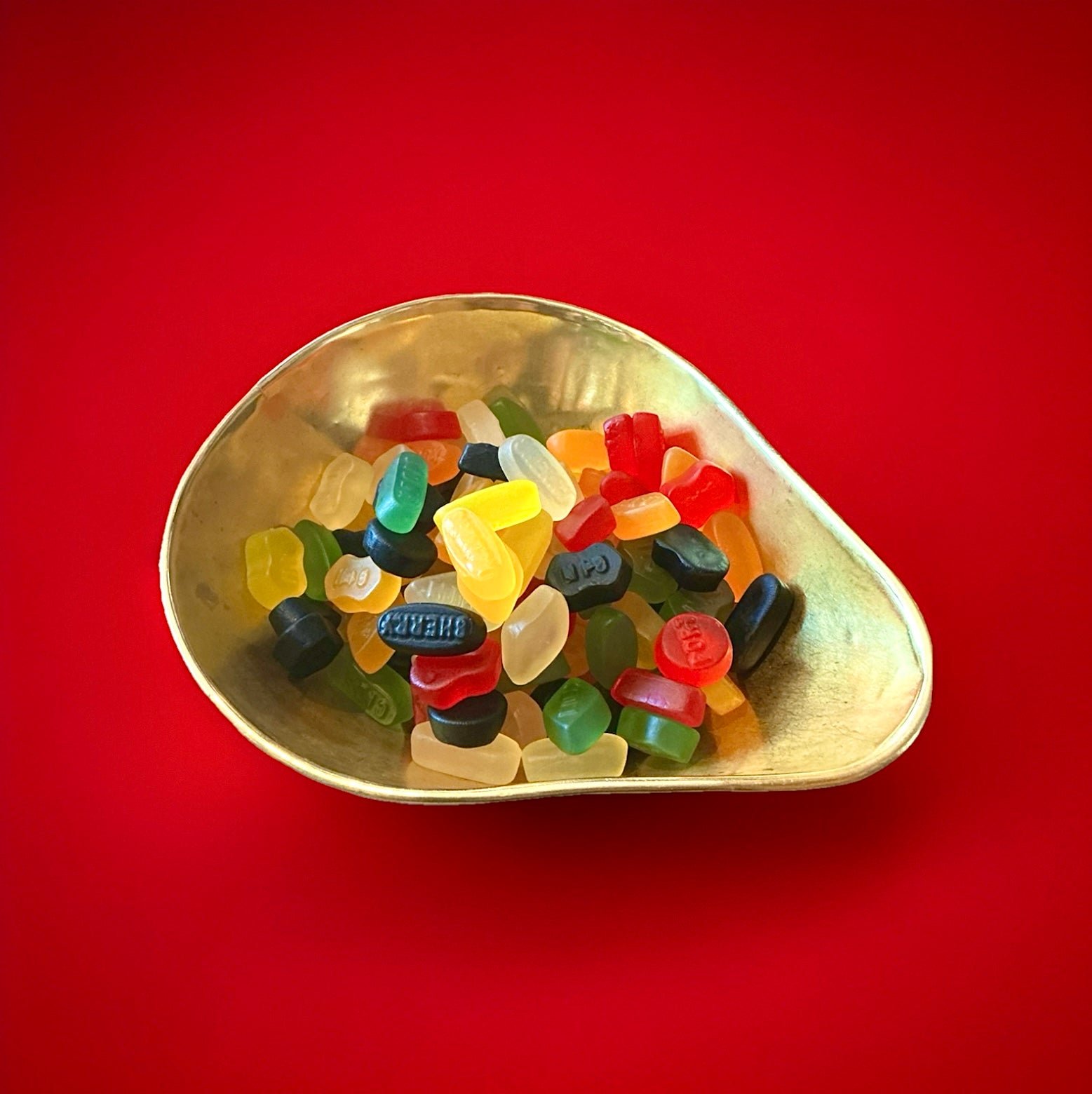 A selection of multicoloured wine gums in a gold bowl on a red background 