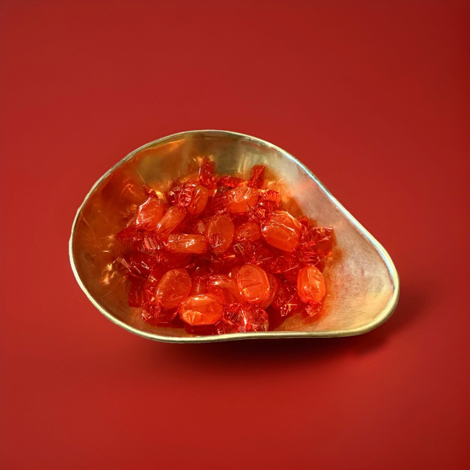 Hard boiled oval shaped throat and chest sweets in an orange wrapper in a gold bowl on a red background 