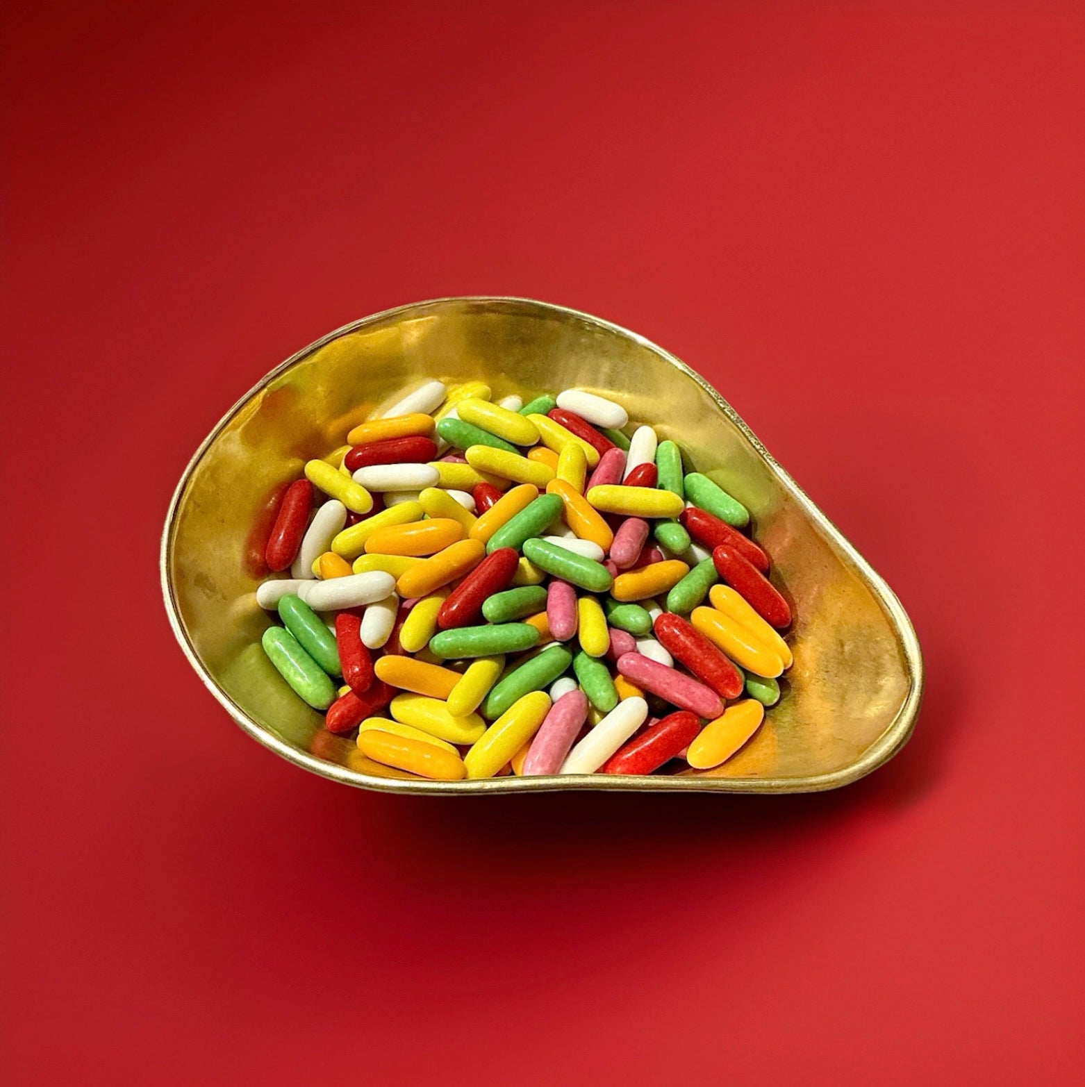 Multicoloured liquorice torpedoes in a gold bowl on a red background 