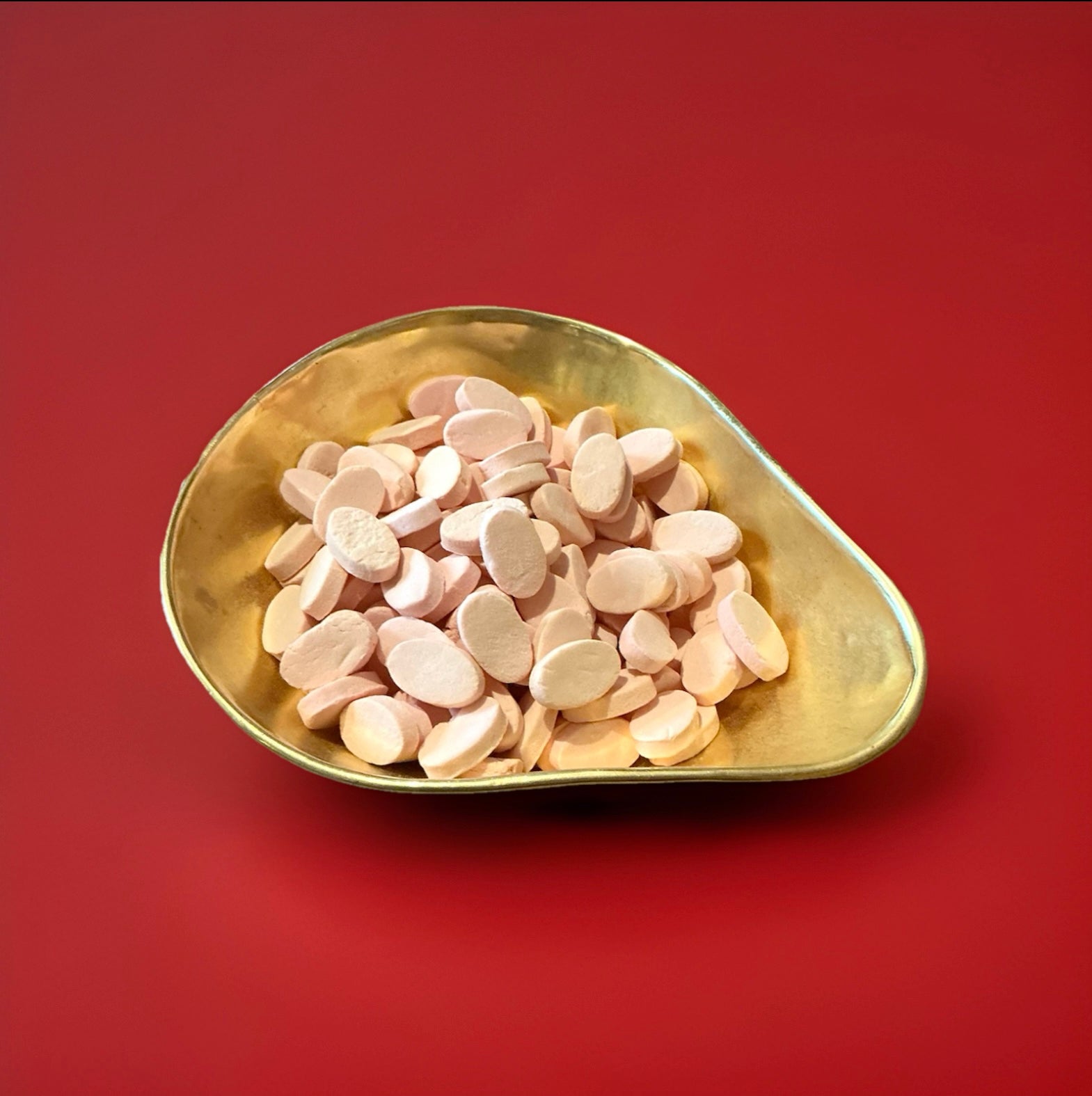 Cinnamon odd fellows are oval shaped chalky discs with a cinnamon flavoured in a gold bowl with a red background 