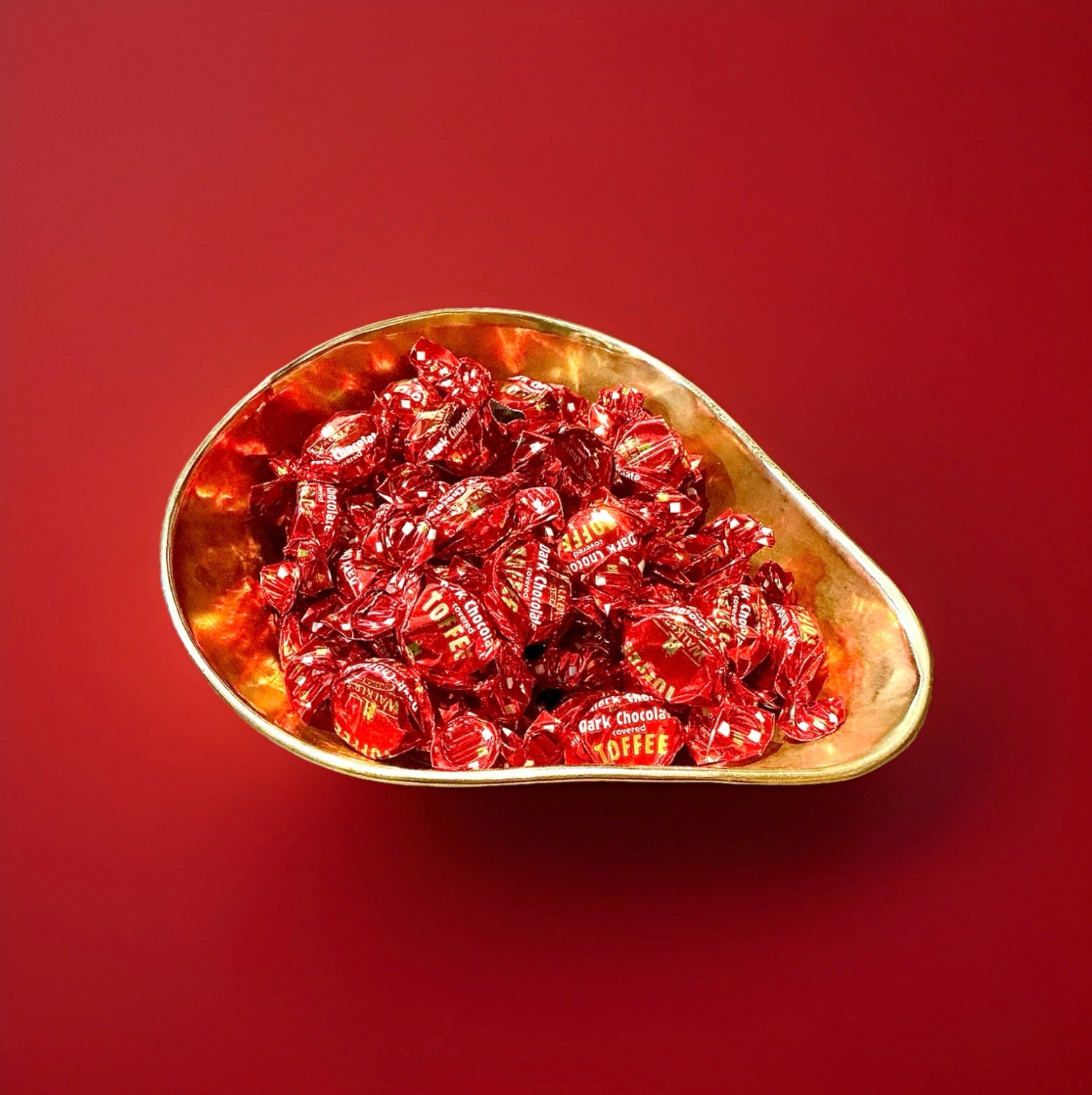Individually wrapped red dark chocolate covered toffees in a gold bowl on a red background