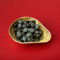 Discs of soft black liquorice Pontefract cakes in a gold bowl on a red background 