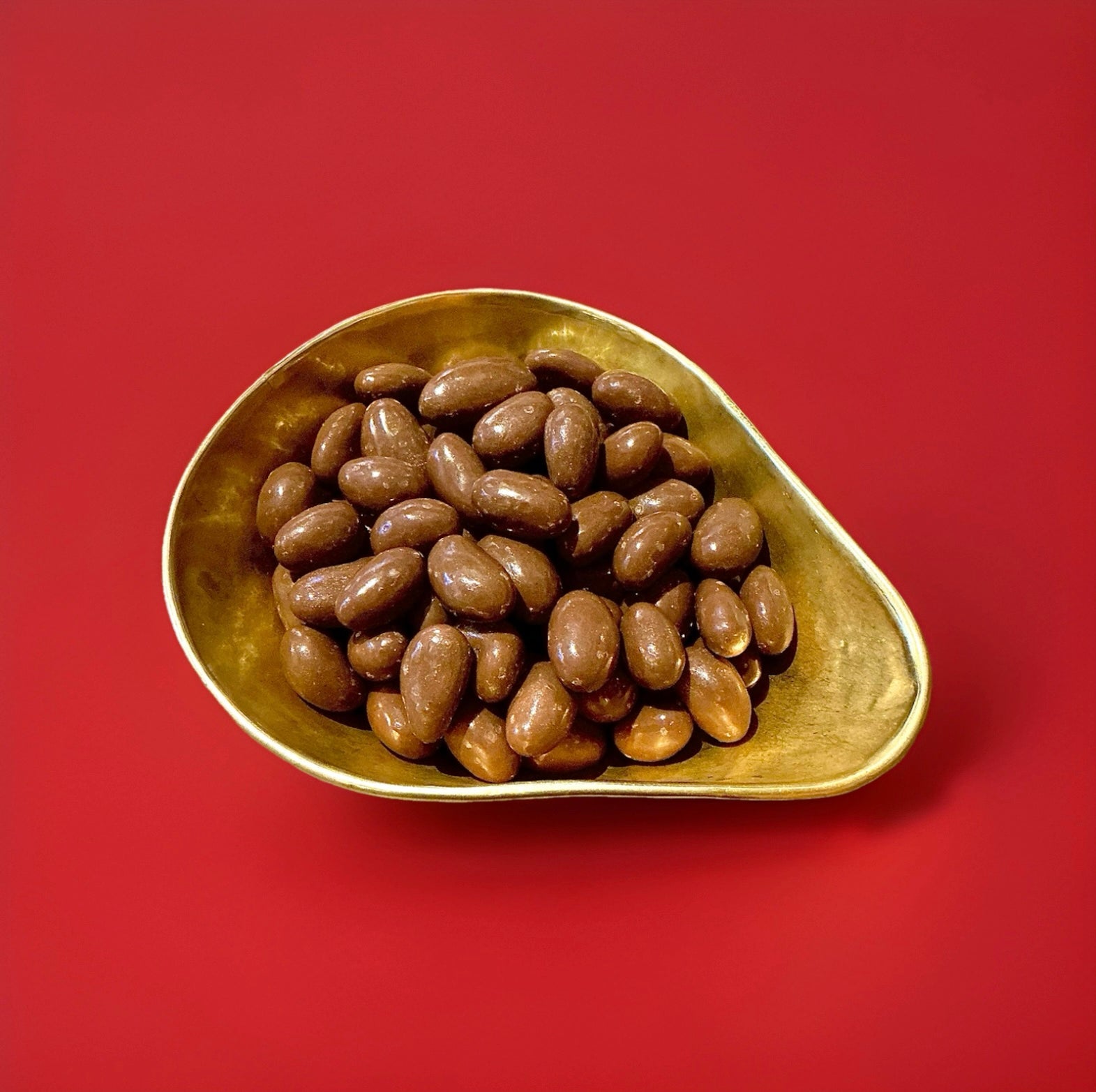 Chocolate coated Brazil nuts in a gold bowl on a red background 