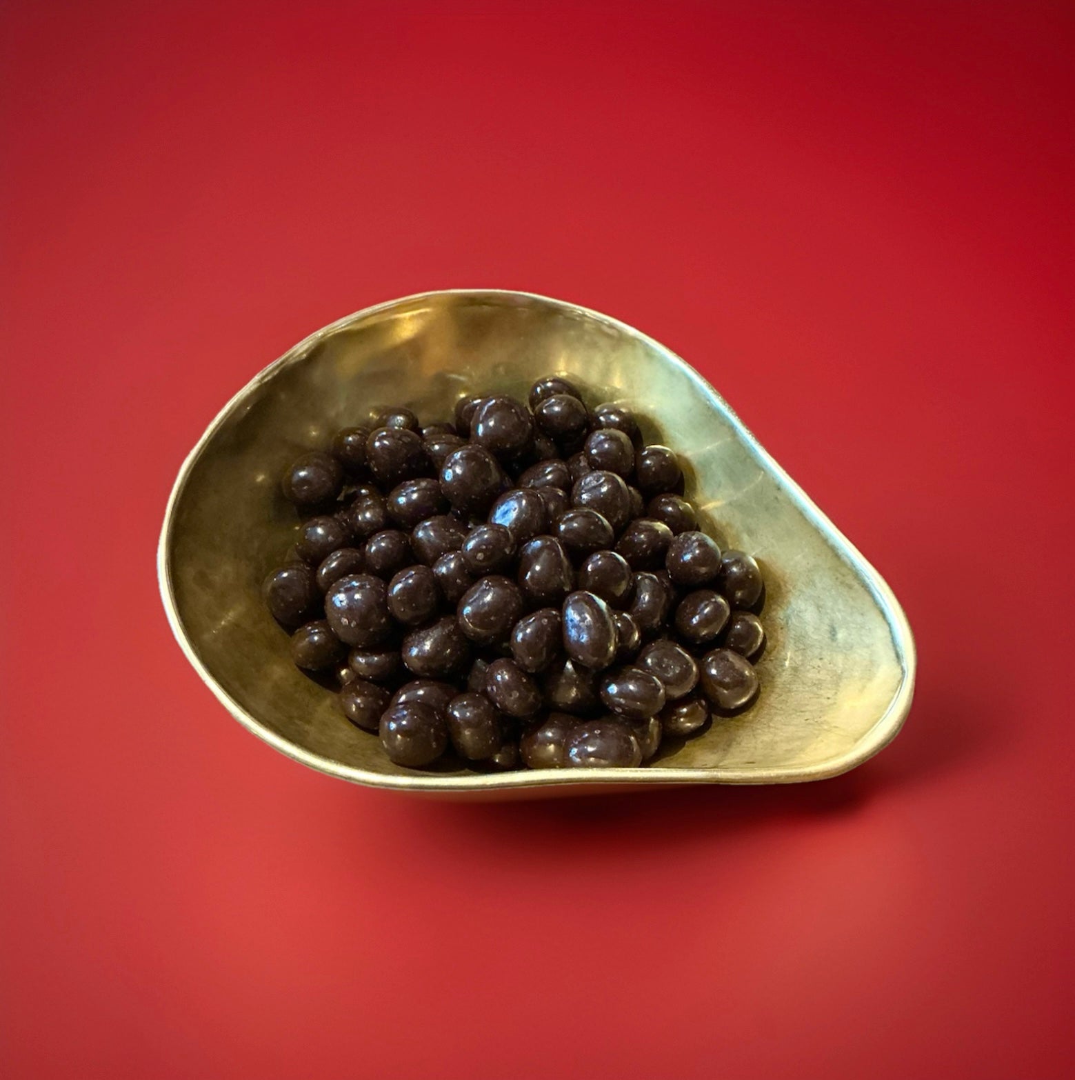 Bite sized pieces of candied ginger coated in dark chocolate in a gold bowl on a red background 