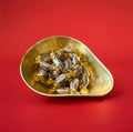 Individually wrapped brown striped mint humbugs in a gold bowl on a red background 