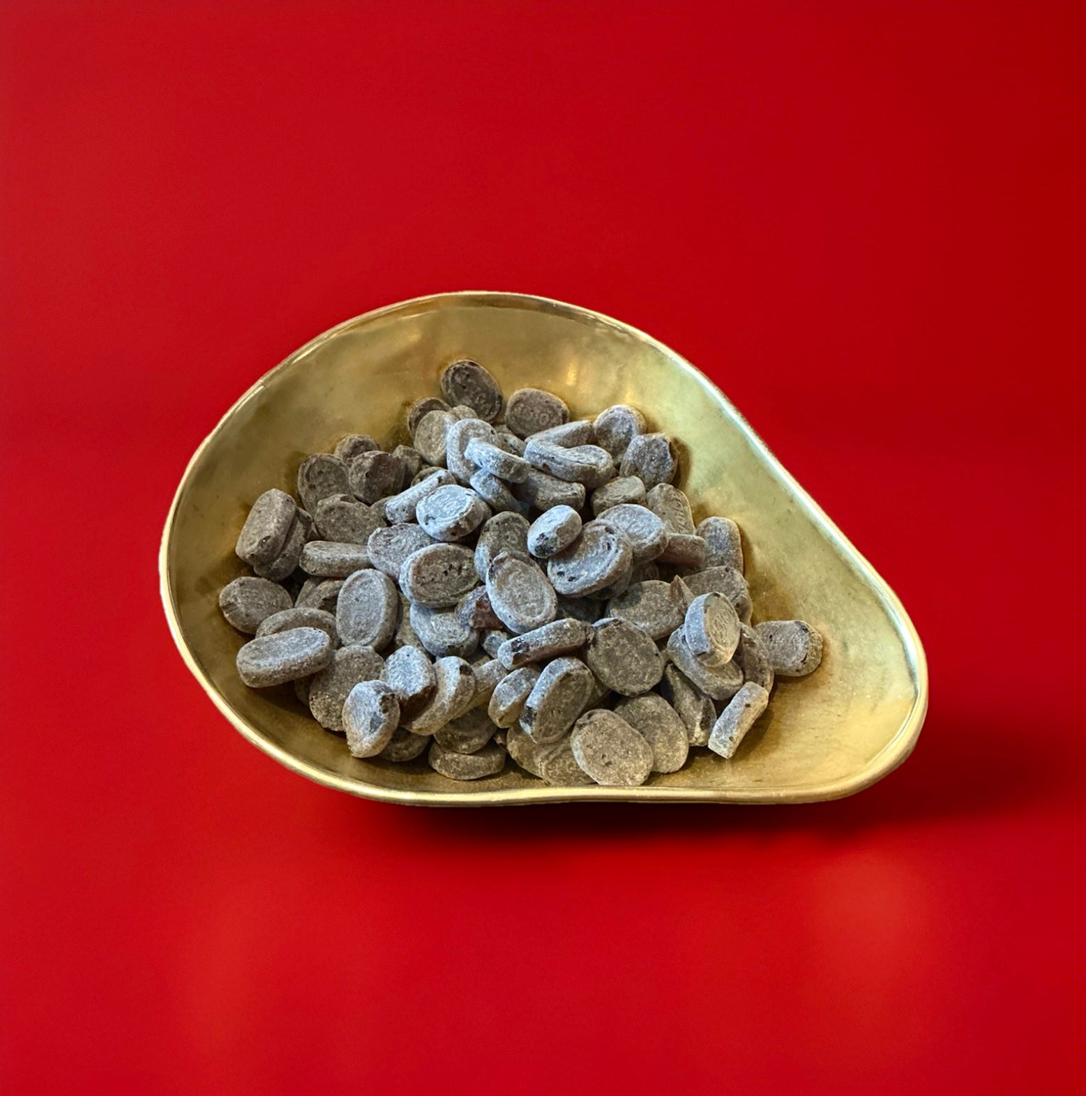 Oval shaped hard boiled voice tablets in a gold bowl on a red background 