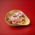 Large red and green strawberry shaped jelly sweets with a sugar coating in. Gold bowl on a red background 