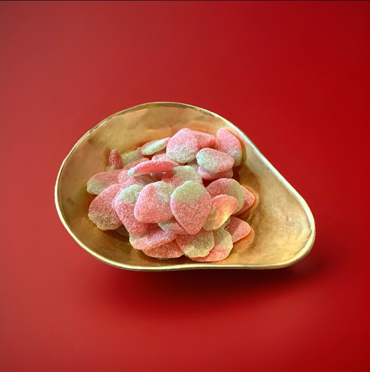 Large red and green strawberry shaped jelly sweets with a sugar coating in. Gold bowl on a red background 