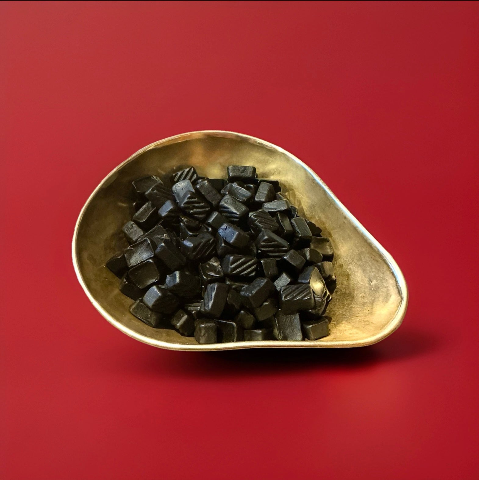 Square shaped lion hard liquorice gums liquorice tablets in a gold bowl with a red background 