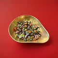Liquorice satins are a cushion shaped liquorice flavoured shell with a liquorice centre made by Gibb in a gold bowl with a red background 
