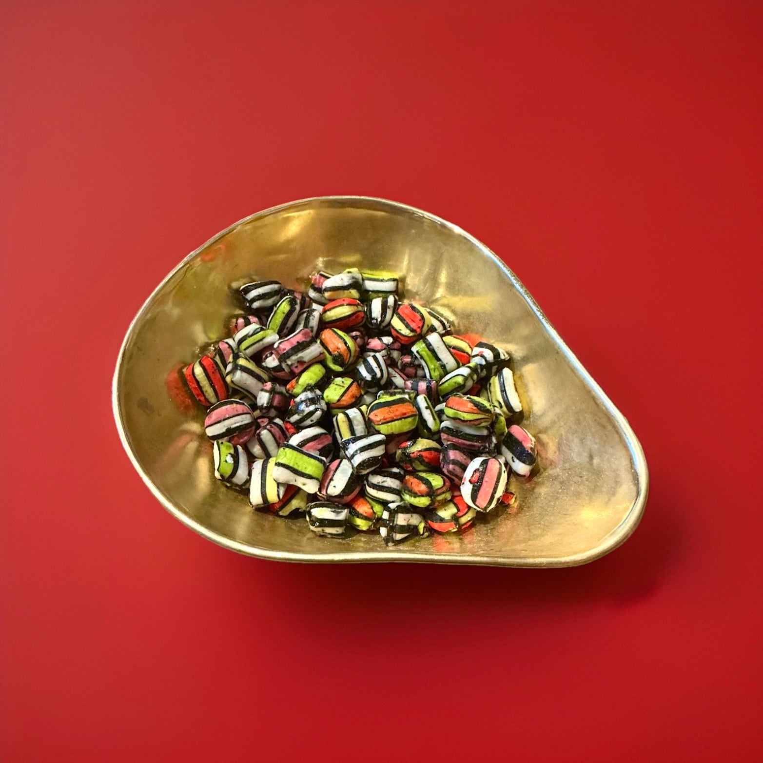 Liquorice satins are a cushion shaped liquorice flavoured shell with a liquorice centre made by Gibb in a gold bowl with a red background 