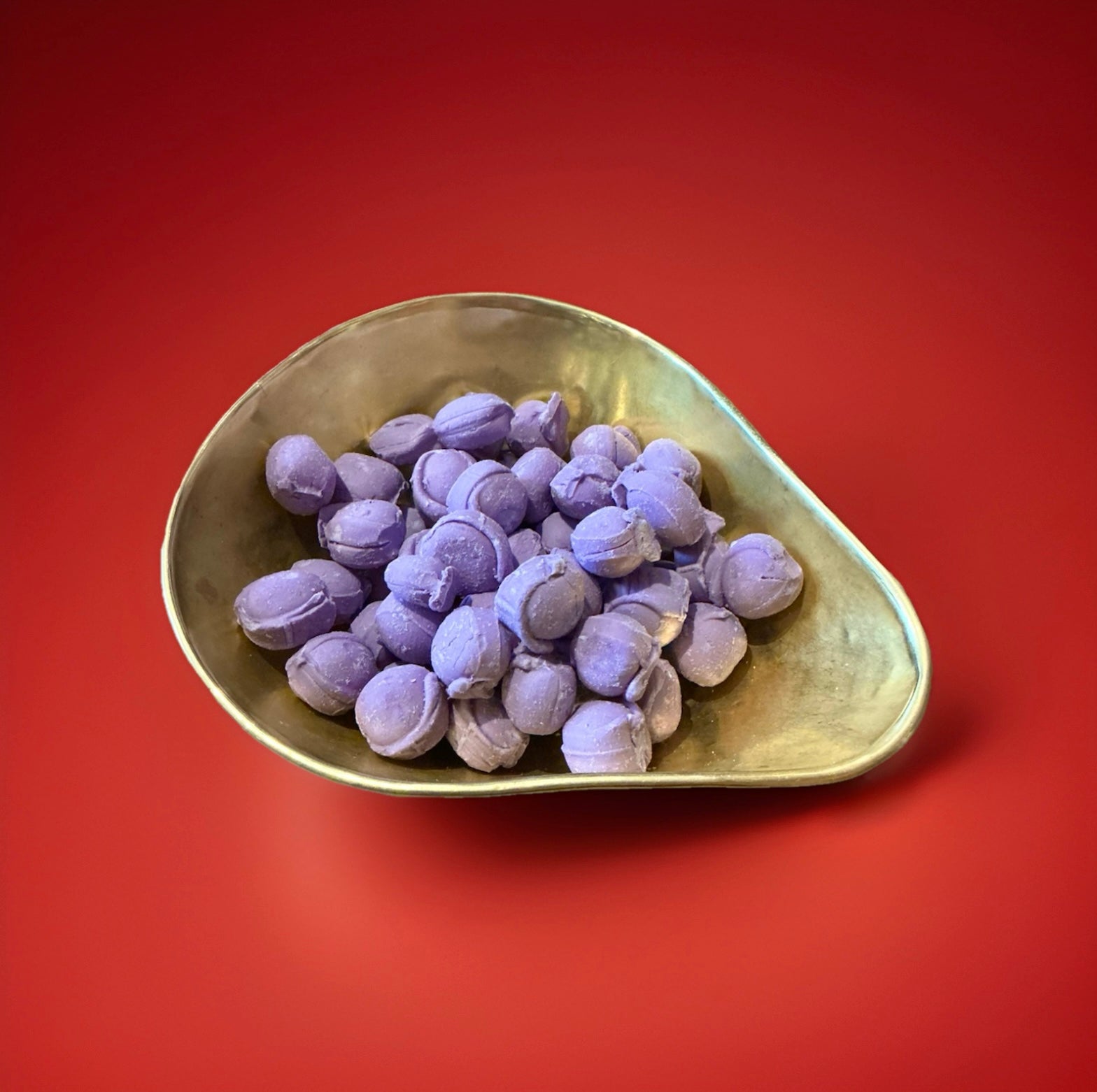 Purple coloured Parma violet flavoured oval shaped sweets in a gold bowl on a red background 