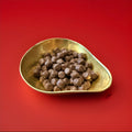 Bite sized pieces of black liquorice coated in milk chocolate in a gold bowl with a red background 
