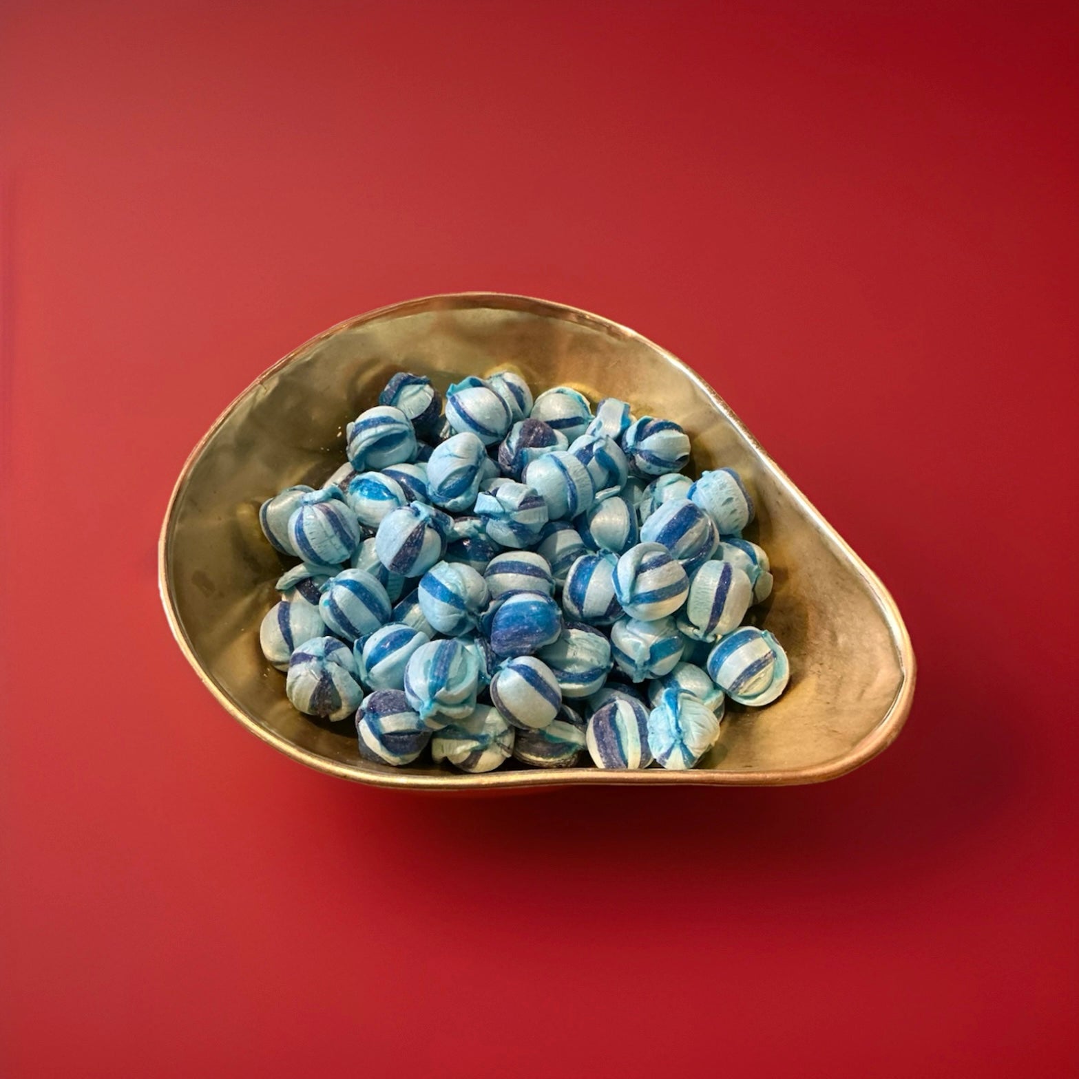 Round hard boiled blue raspberry flavoured sweets dark and light blue stripes in a gold bowl with a red background 