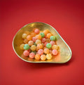 Multicoloured hard boiled round sweet mixed fruit flavours covered in malic acid in a gold bowl on a red background 