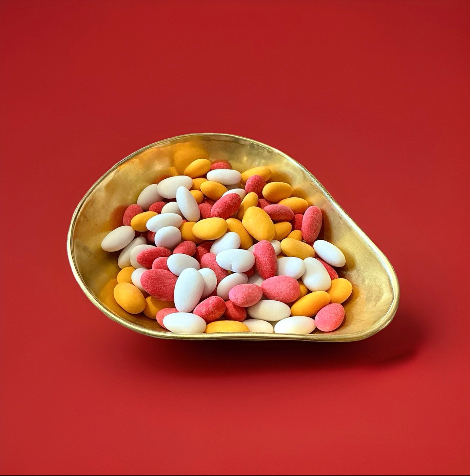 Multicoloured sugared almonds in a gold bowl on a red background 