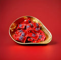 Individually wrapped uncle joes mint balls in red packaging in a gold bowl on a red background 