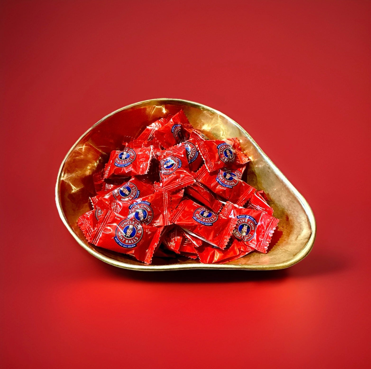 Individually wrapped uncle joes mint balls in red packaging in a gold bowl on a red background 