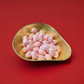 Light pink coloured floral flavoured oval shaped soft rock sweets in a gold bowl on a red background 