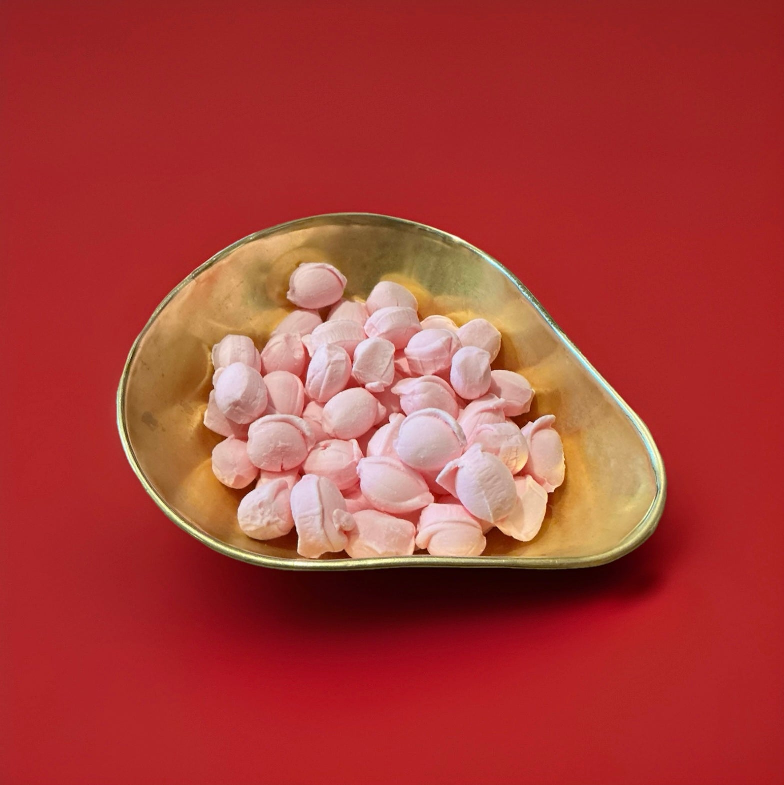Light pink coloured floral flavoured oval shaped soft rock sweets in a gold bowl on a red background 