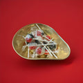 Individually wrapped red white and black lolly with a paper stick in a gold bowl with a red background 