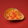 Yellow and orange coloured soft jelly peaches with a sugar coating in a gold bowl on a red background 