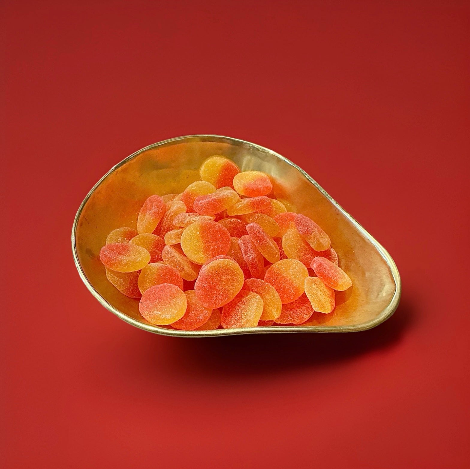 Yellow and orange coloured soft jelly peaches with a sugar coating in a gold bowl on a red background 