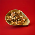 Chunks of buttered Brazil brittle pieces in a gold bowl with a red background 