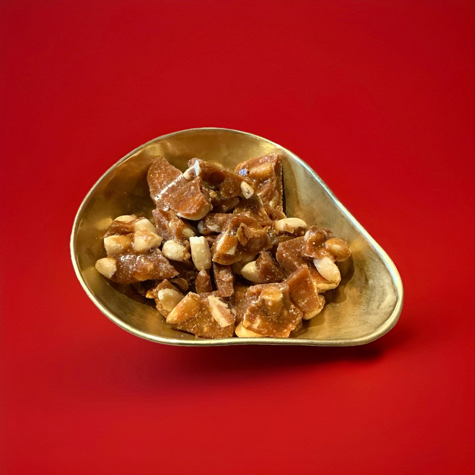 Chunks of buttered Brazil brittle pieces in a gold bowl with a red background 