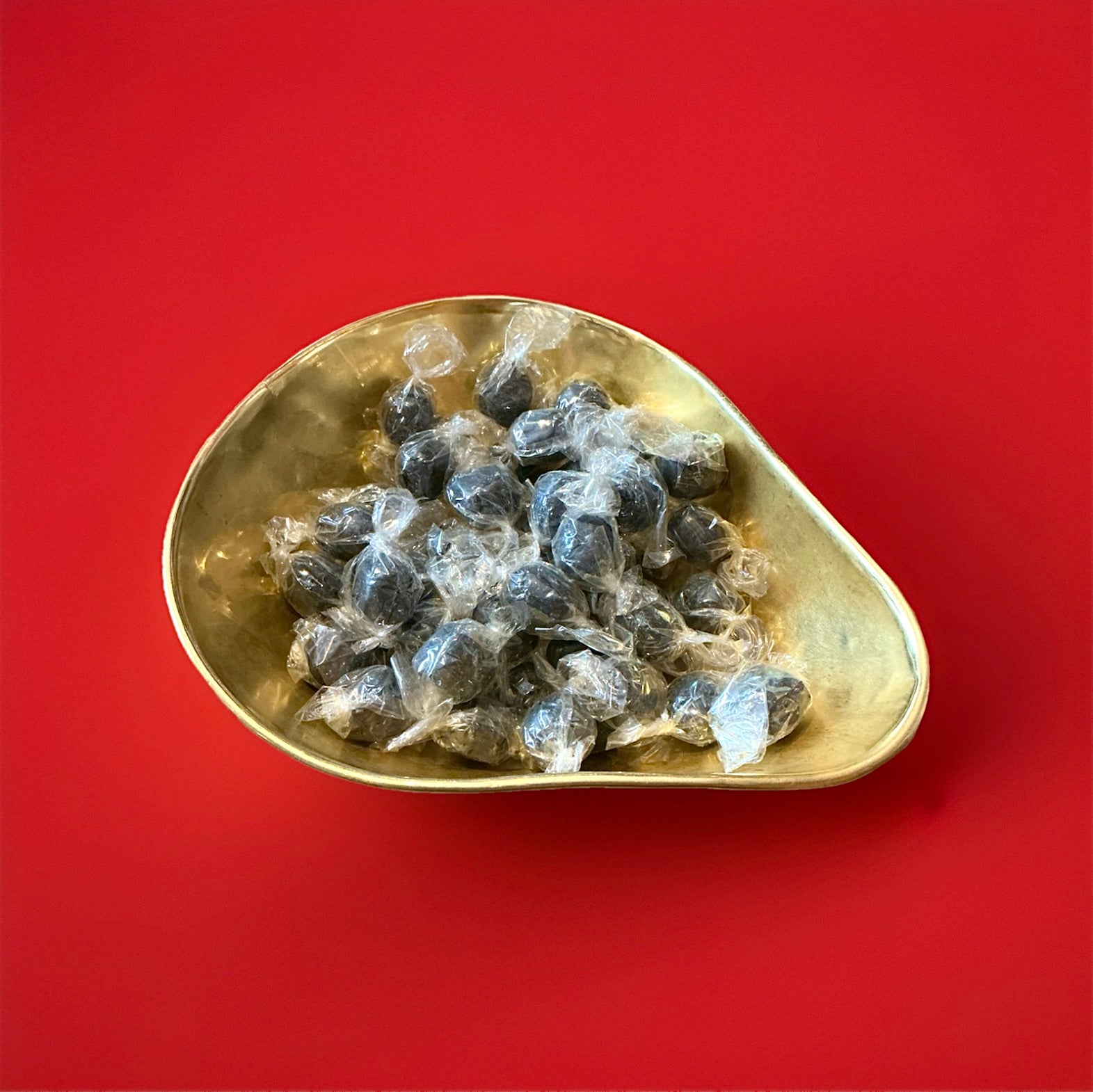 Individually wrapped hard boiled brown coloured black bullet mints in a gold bowl on a red background 