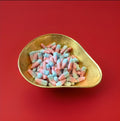 Pink and blue bottle shaped jelly sweets with a fizzy sugar coating and bubblegum flavour in a gold bowl with a red background 