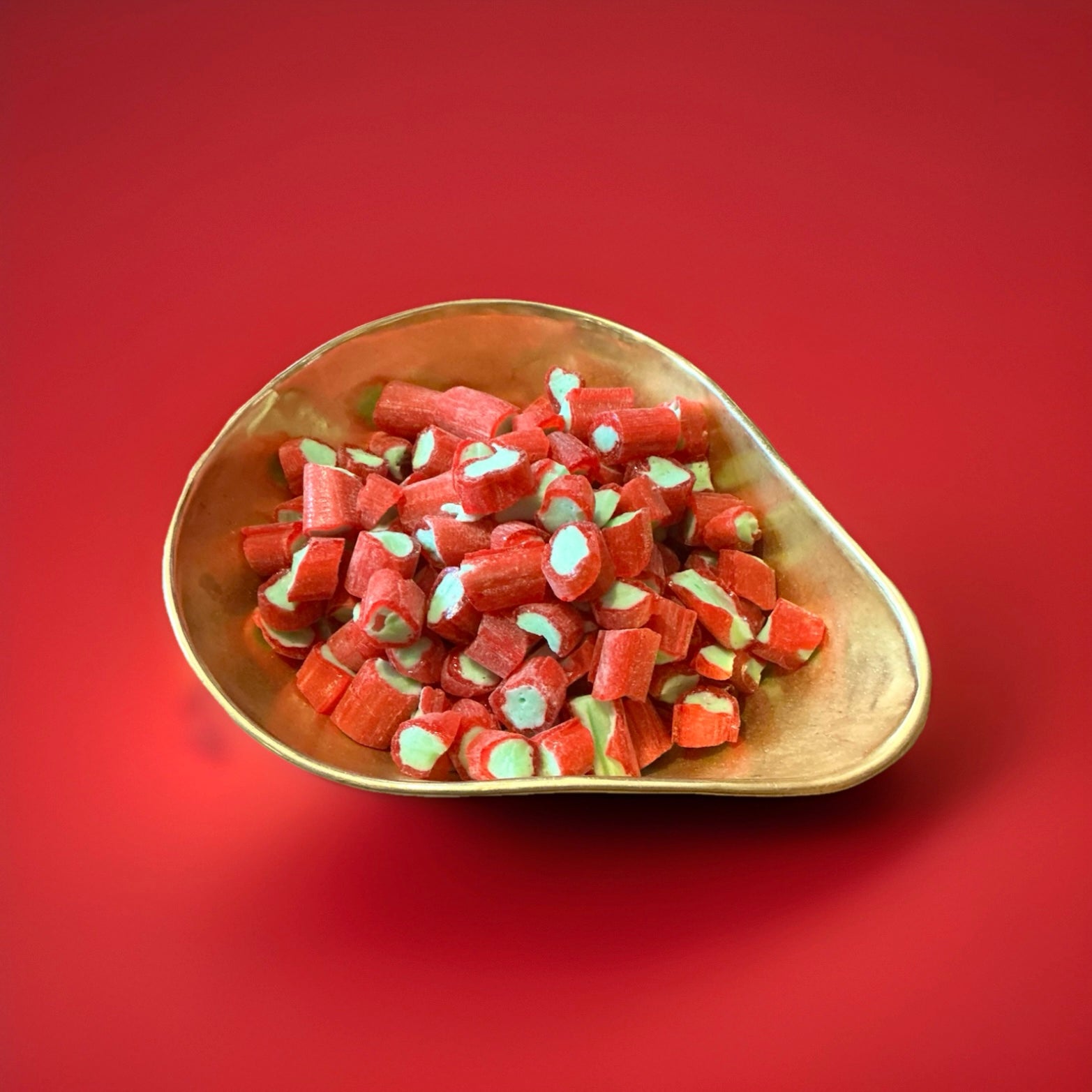Red and green rhubarb flavoured rock cuttings in a gold bowl with a red background 