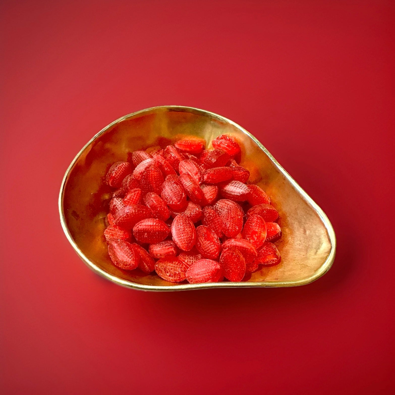Red hard boiled oval shaped strawberry flavoured sweets with a sherbet centre in a gold bowl on a red background 
