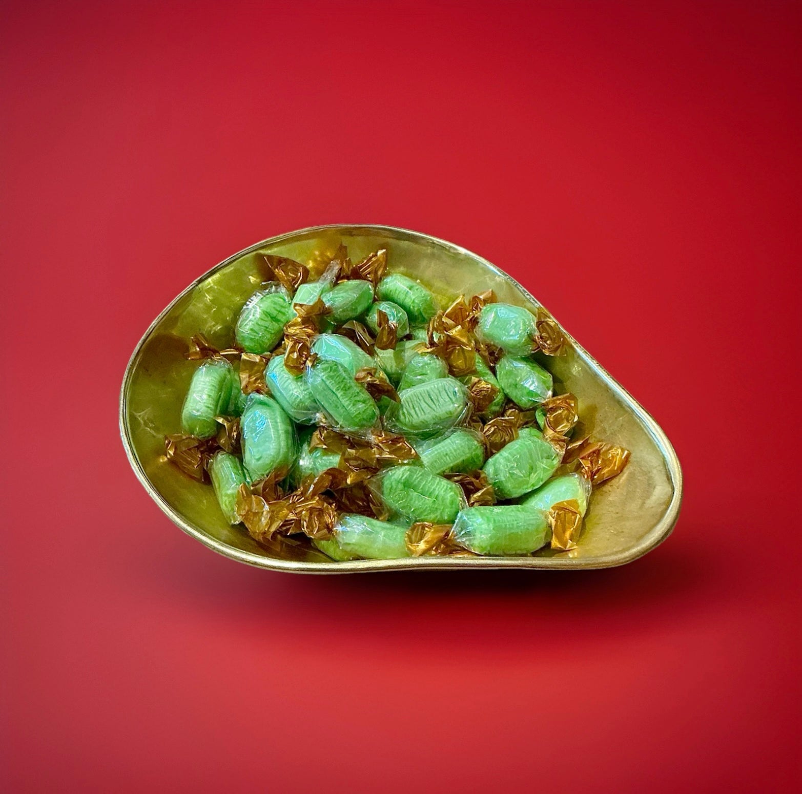 Individually wrapped green chocolates lime sweets in a gold bowl on a red background 