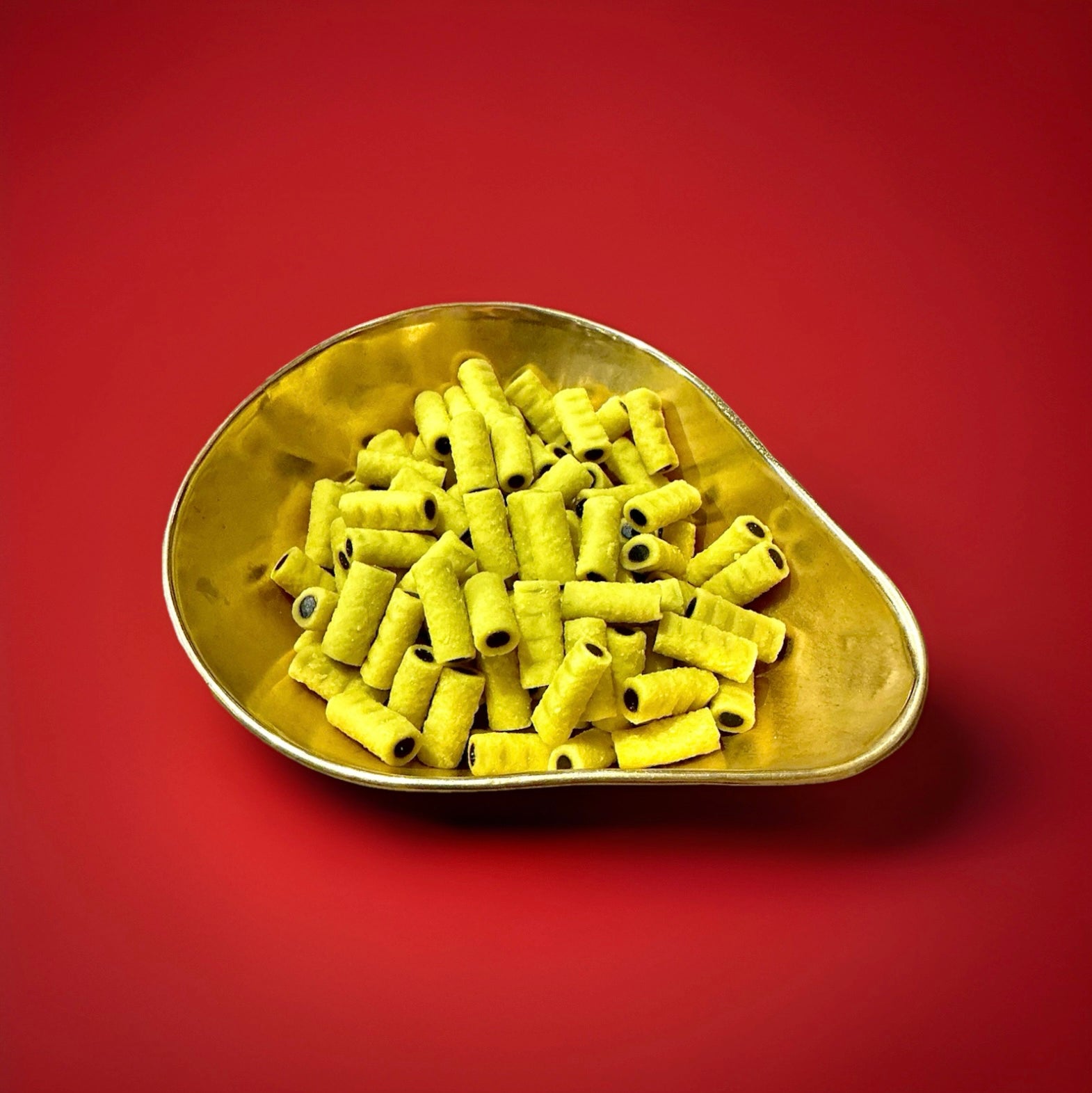 Yellow coconut roll with a black liquorice centre in a gold bowl on a red background 