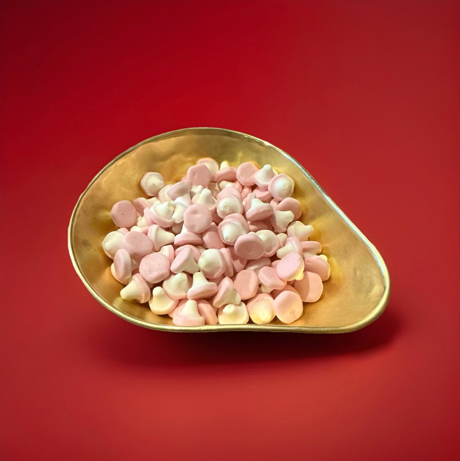 Pink and white coloured foam mushroom sweets in a gold bowl on a red background 
