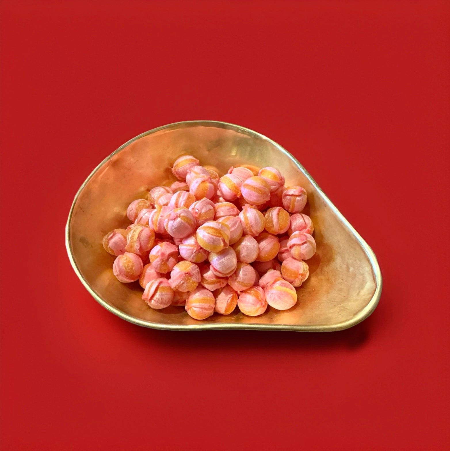Pink and orange striped round hard boiled sweets with a floral flavour in a gold bowl with a red background 