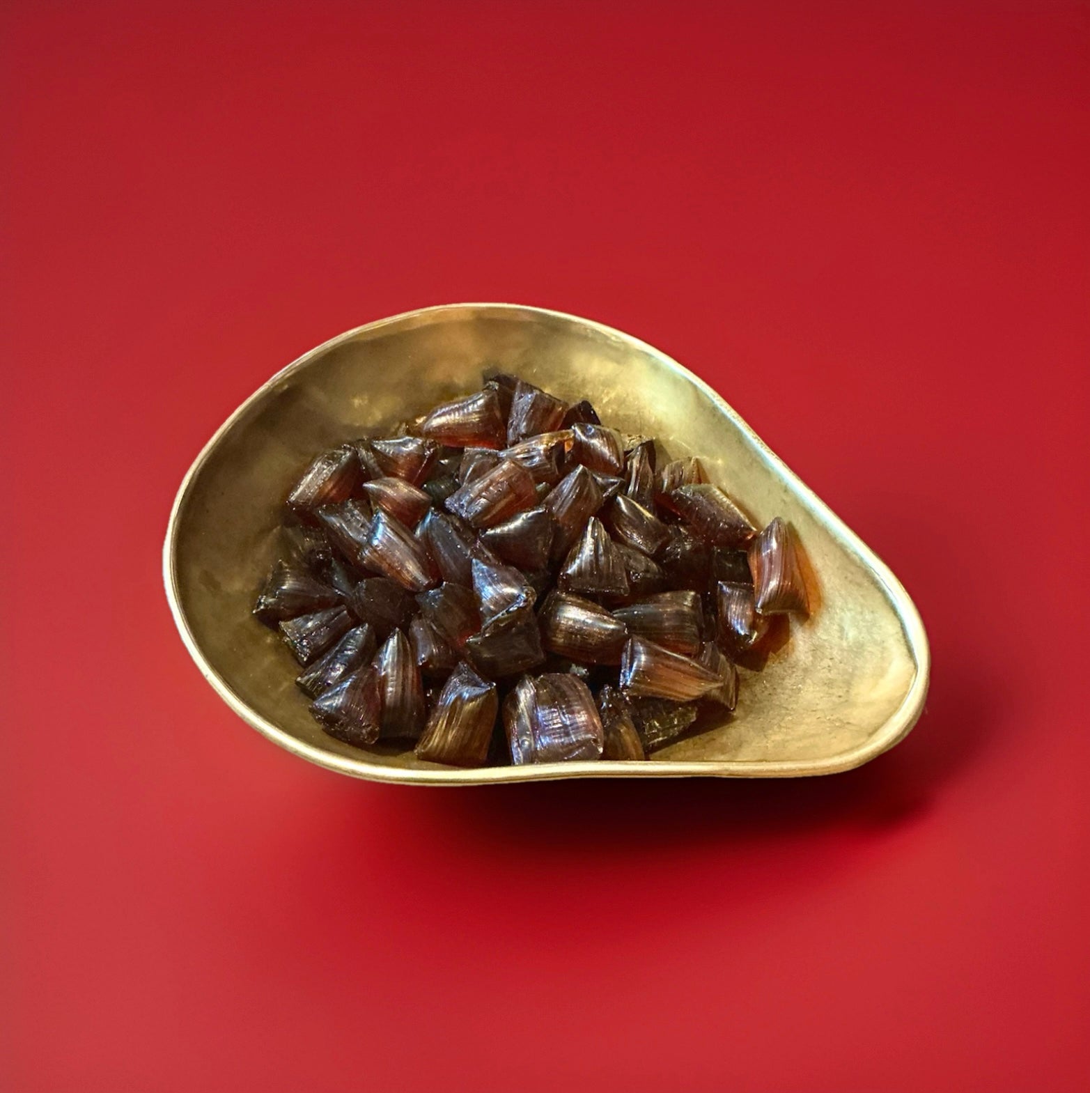 Rich buttery caramelised toffee hard boiled sweets in a gold bowl with a red background 