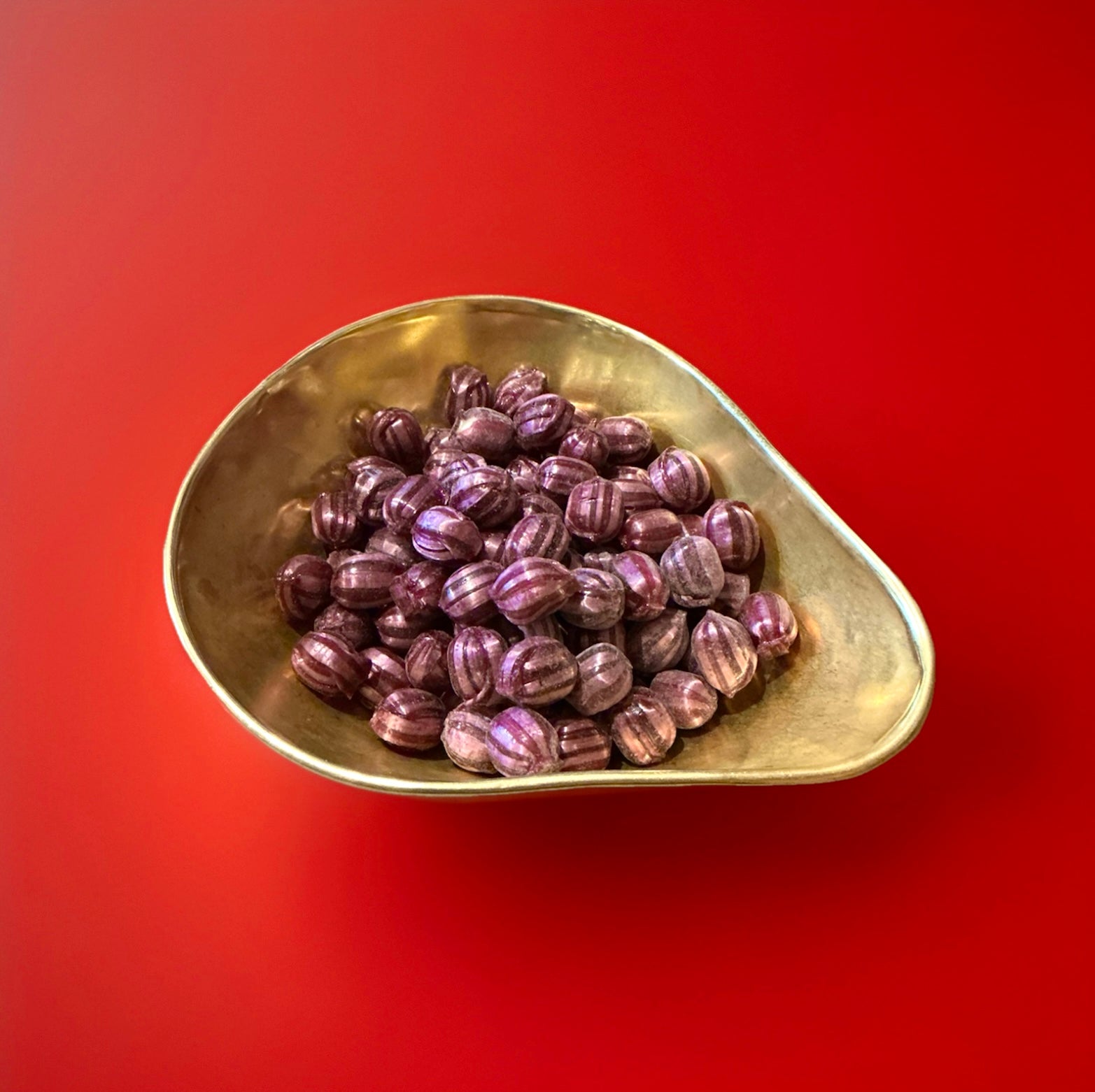 Light and dark striped round boiled sweets with a grape flavour and a fizzy sherbet centre in a gold bowl with a red background 