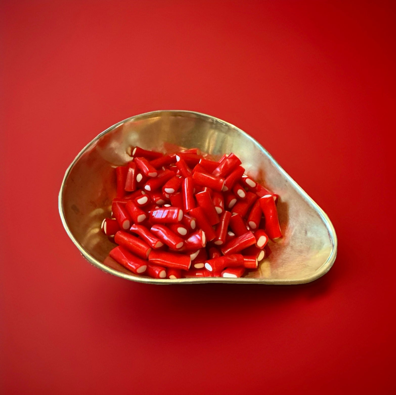 Red strawberry flavoured liquorice tubes filled with white fondant in a gold bowl on a red background 