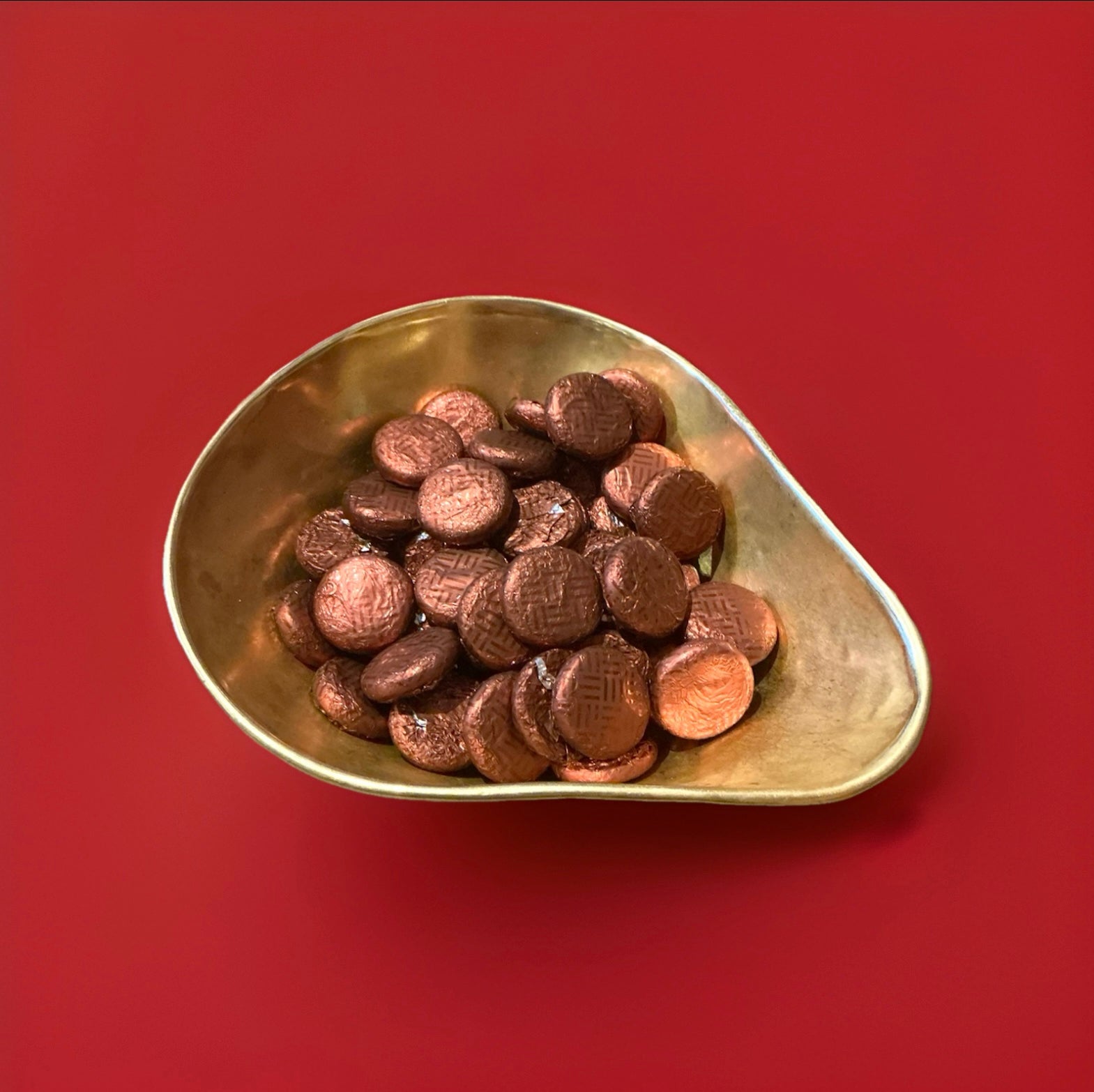 Coffee creams are individually wrapped in brown foil the disc shaped sweet is coffee fondant wrapped in chocolate in a gold bowl with a red background 