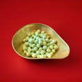 Round shaped Green coloured apple flavoured Bon Bon’s in a gold bowl on a red background 